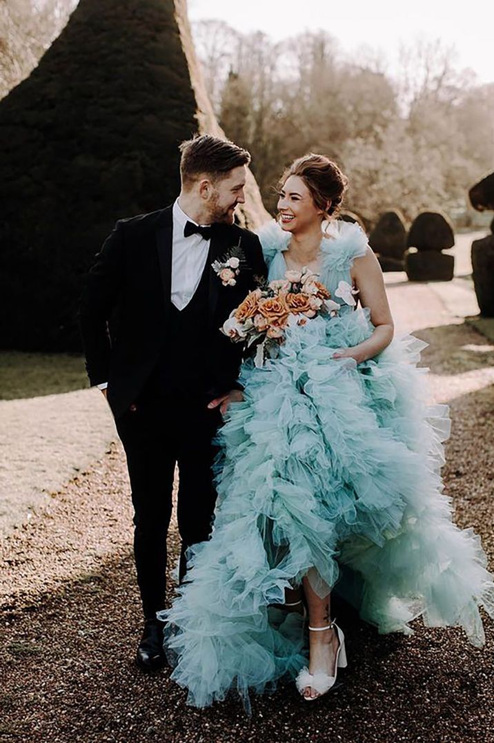 Bride wearing a unique blue ruffle wedding dress walking arm in arm with the groom by Gail Secker Photography