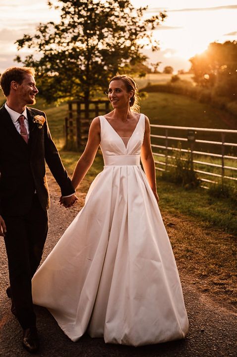 Golden hour portrait with bride in a fit and flare wedding dress holding hands with her groom 