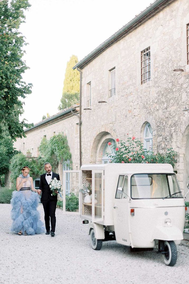 Bride in pale blue wedding dress and groom in black tie next to cream Tuk Tuk wedding transport