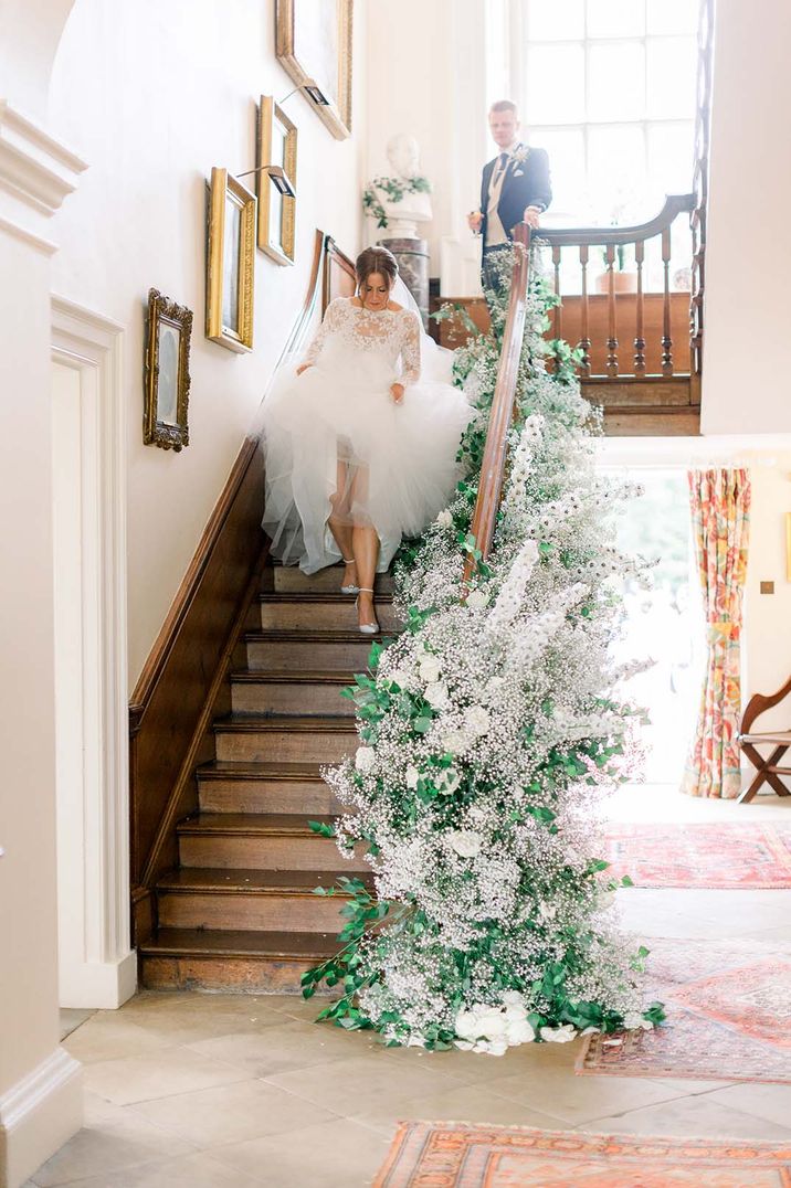 Staircase at country house wedding venue with large neutral toned floral decorations up the side