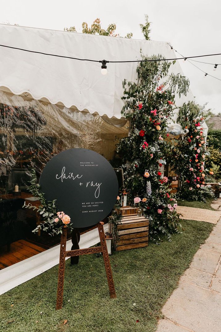 Circular chalk board wedding sign with fairy lights and rose and eucalyptus floral decorations 