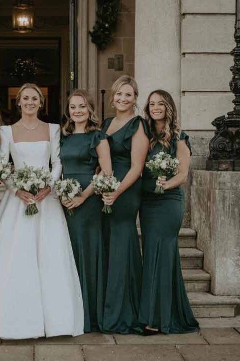 Bride in classic square neck long sleeve wedding dress standing with bridesmaids in bottle green mismatched bridesmaid dresses at Hedsor House