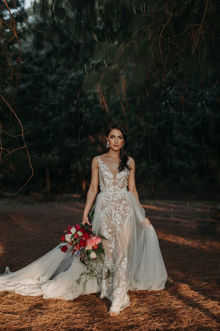 Bride with long brown side swept hair in the woods in a fitted lace wedding dress with plunging neckline and detachable chiffon skirt 