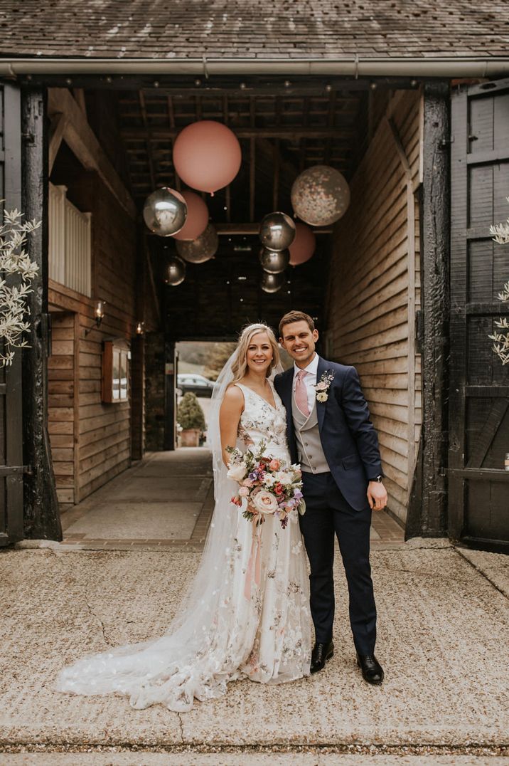 Spring Prezola wedding couple in a floral embroidered wedding dress and navy suit standing in the courtyard of their wedding venue 