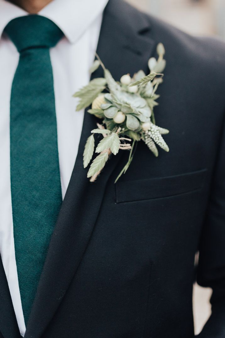 Groom in a black suit with green tie and foliage buttonhole 