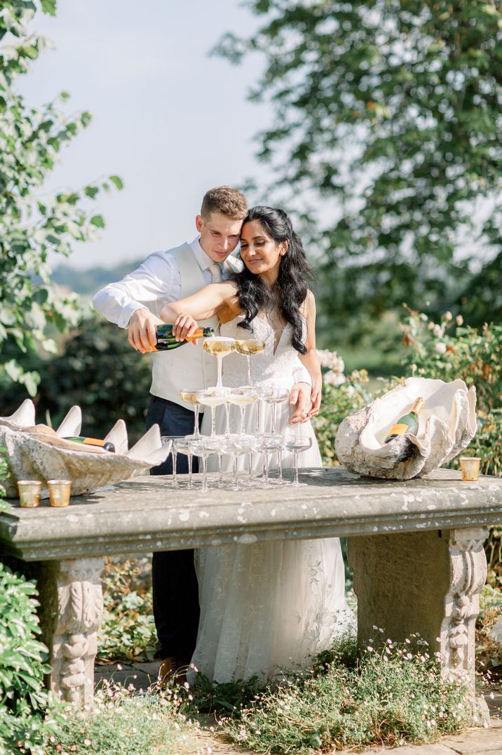 Couple pour champagne into glass tower on their wedding day at traditional wedding