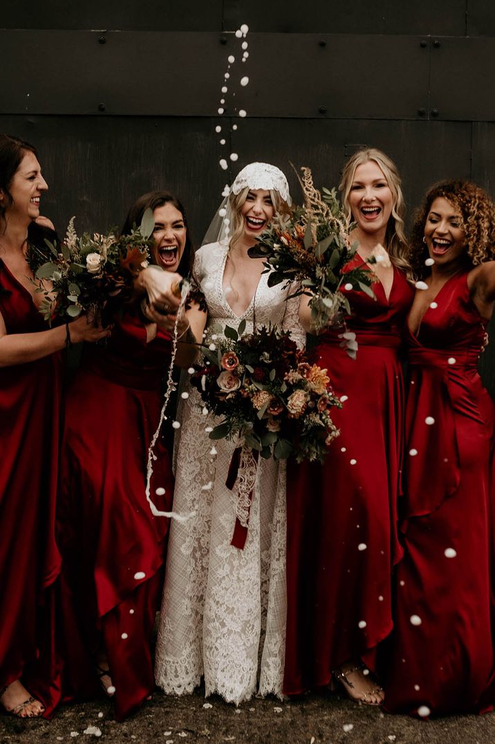 Bridal party champagne pop picture with dark red bridesmaid dresses and lace wedding dress and Juliet cap veil