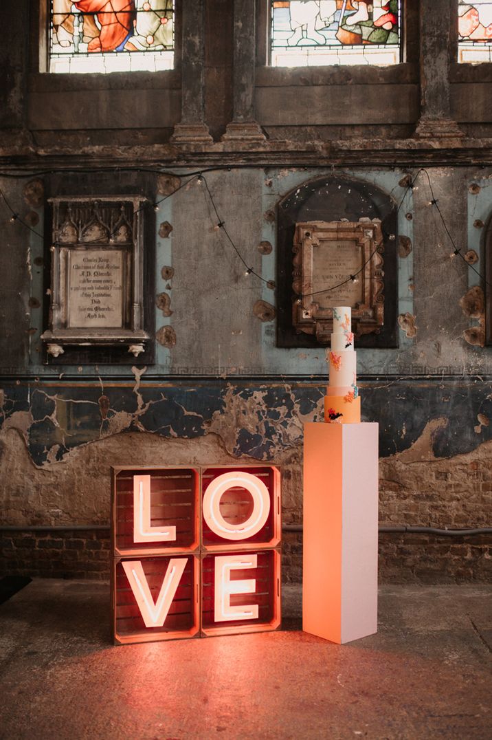 Pink 'LOVE' neon wedding sign next to colourful wedding cake 