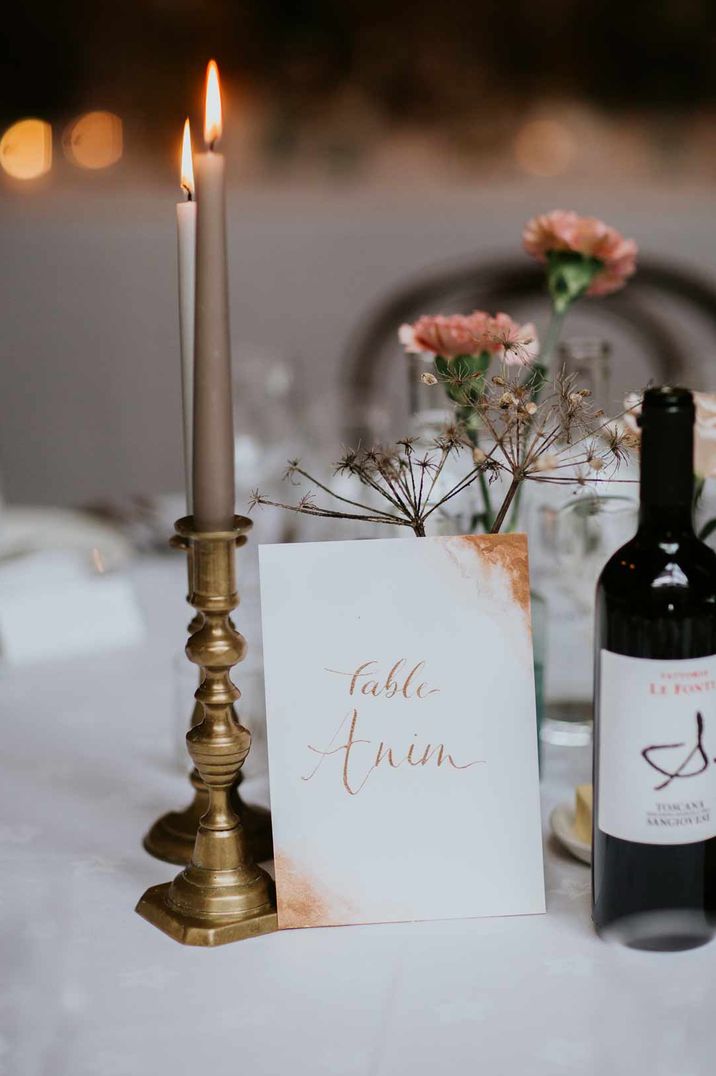 Brown and taupe taper candles in gold holders with signs for the table names in Tagalog with mixed gender wedding party