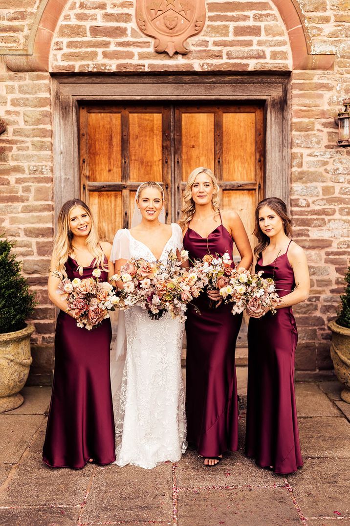 Bridesmaids in burgundy satin bridesmaid dresses with the bride for the classic country house wedding 