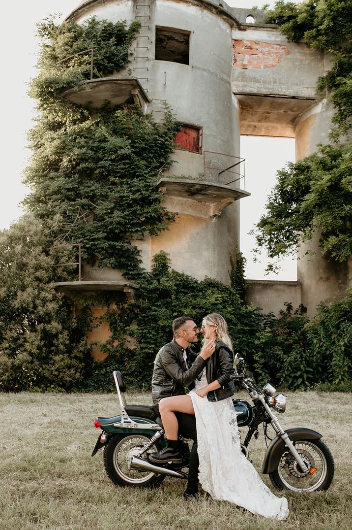 Groom in leather jacket on motorbike with the bride in a leather jacket and lace wedding dress 