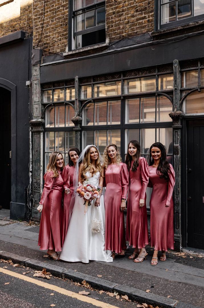 Bride in satin wedding dress standing in London with bridal party in long sleeve satin bridesmaid dresses 