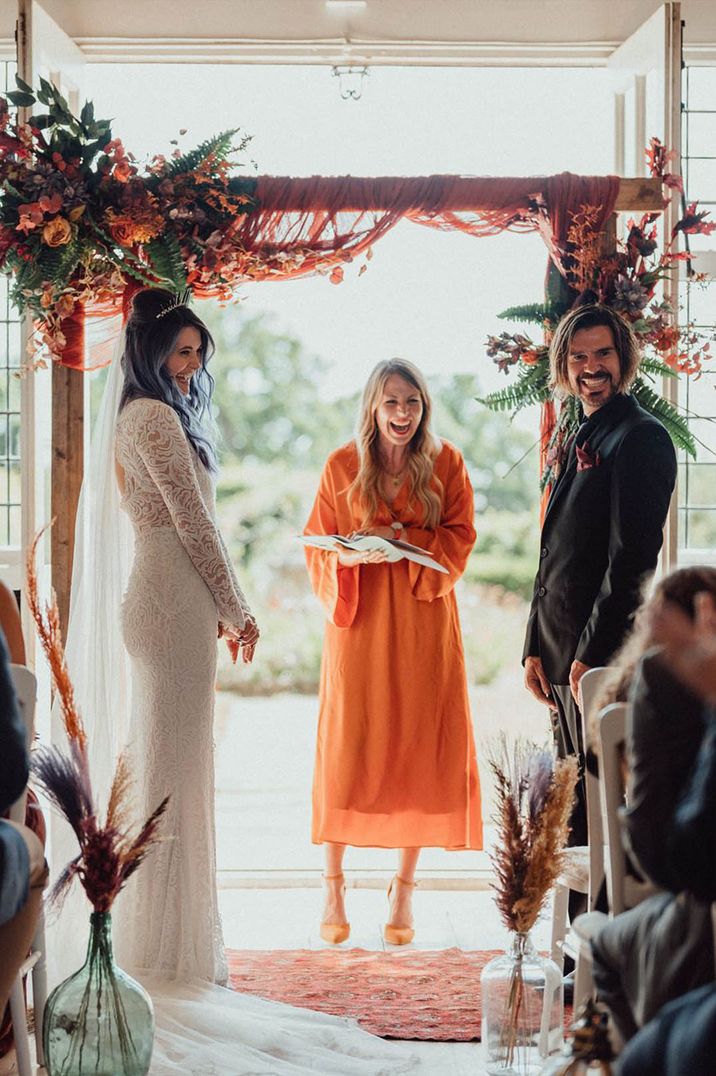 Bride in lace boho wedding dress with groom standing in front of floral altar decoration