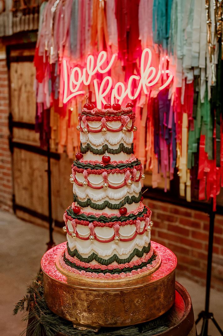 White iced three tier wedding cake with green, pink and red piping with cherry cake topper decoration 