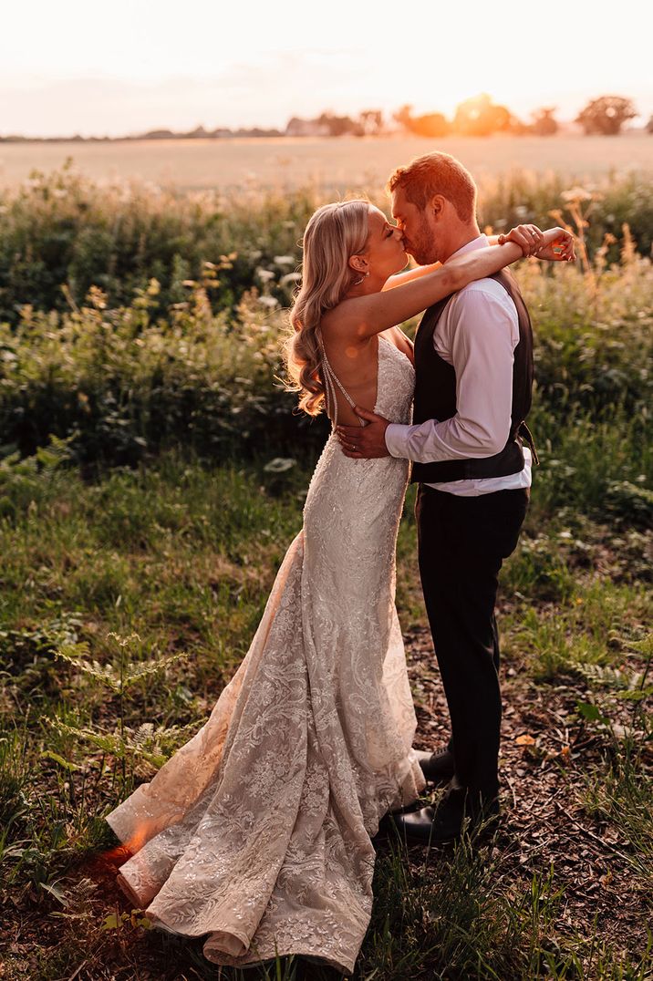 Bride in jewelled sparkly wedding dress reaching up to kiss the groom for golden hour couple portrait 