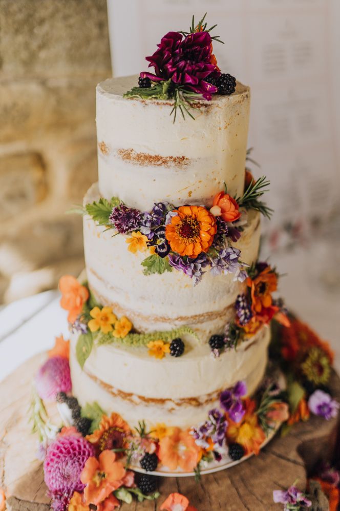 Semi naked wedding cake on a tree slice cake stand decorated with brightly coloured wild flowers 