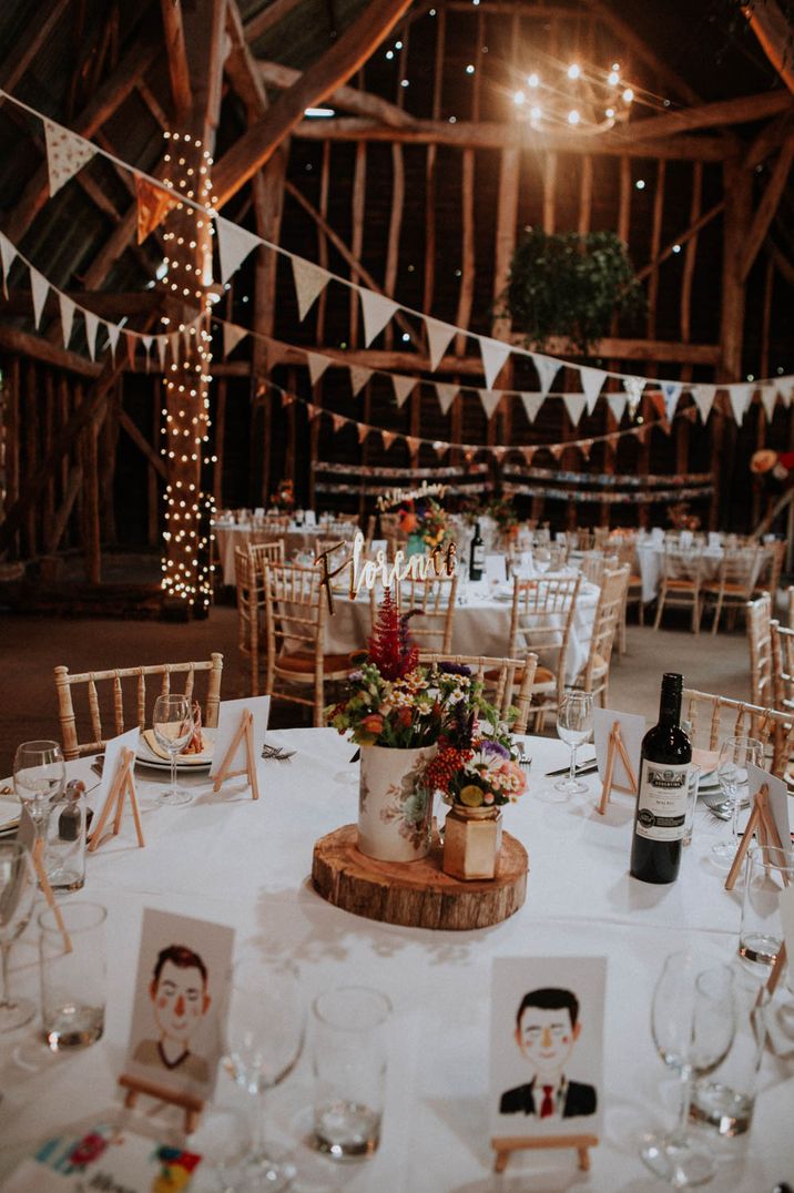 rustic wedding decor in a barn with bunting, fairy lights, tree slice centrepiece and flowers in jars 