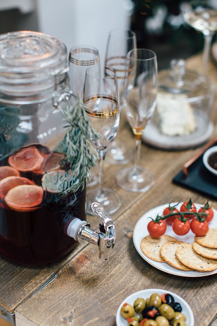 Mulled wine decanter, champagne glasses, vine tomatoes, a block of cheese and crackers at Christmas soiree