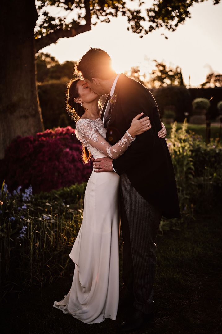 Castle wedding with the bride in long sleeve lace wedding dress with groom sharing a kiss during golden hour 