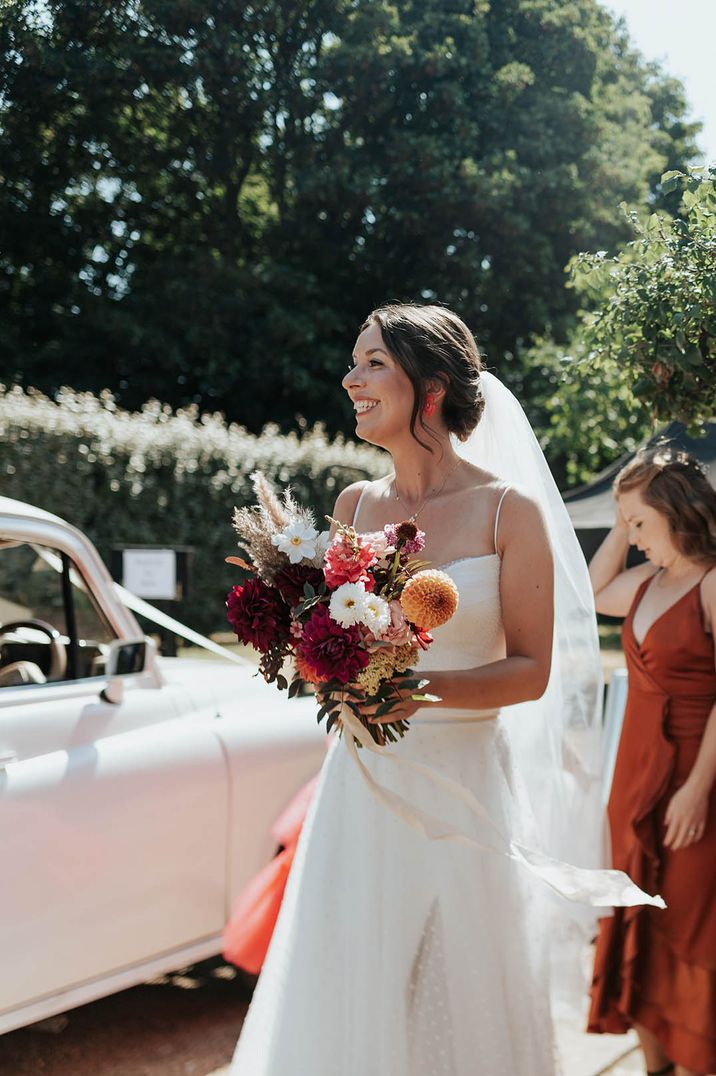 bride in a fitted wedding dress with spaghetti straps holding a colourful flower wedding bouquet 