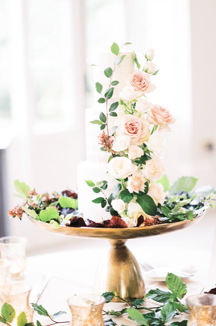 Elegant white iced wedding cake sitting on a gold cake stand with light pink flowers cascading down the front 