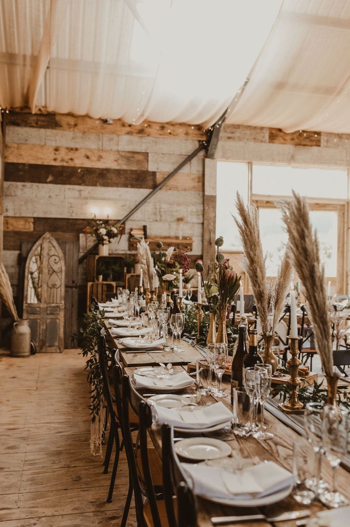 Rustic wedding tablescape with fauna, glass bottles, golden bottles and candlesticks, and neutral toned crockery and napkins