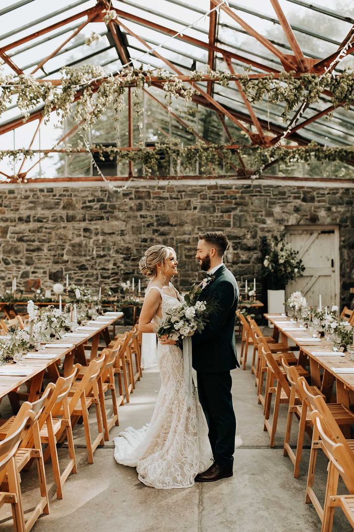 Bride and groom embracing at Plas Dinam country house glasshouse wedding venue with foliage wrapped in the beams 