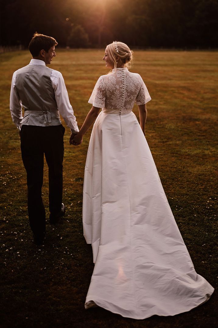 Bride in short sleeve lace wedding dress with sparkly tiara walking along with the groom during golden hour 