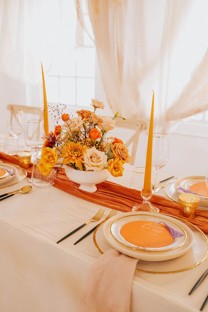 Orange theme wedding with an bright orange tablescape including a table runner, taper candles and flowers 