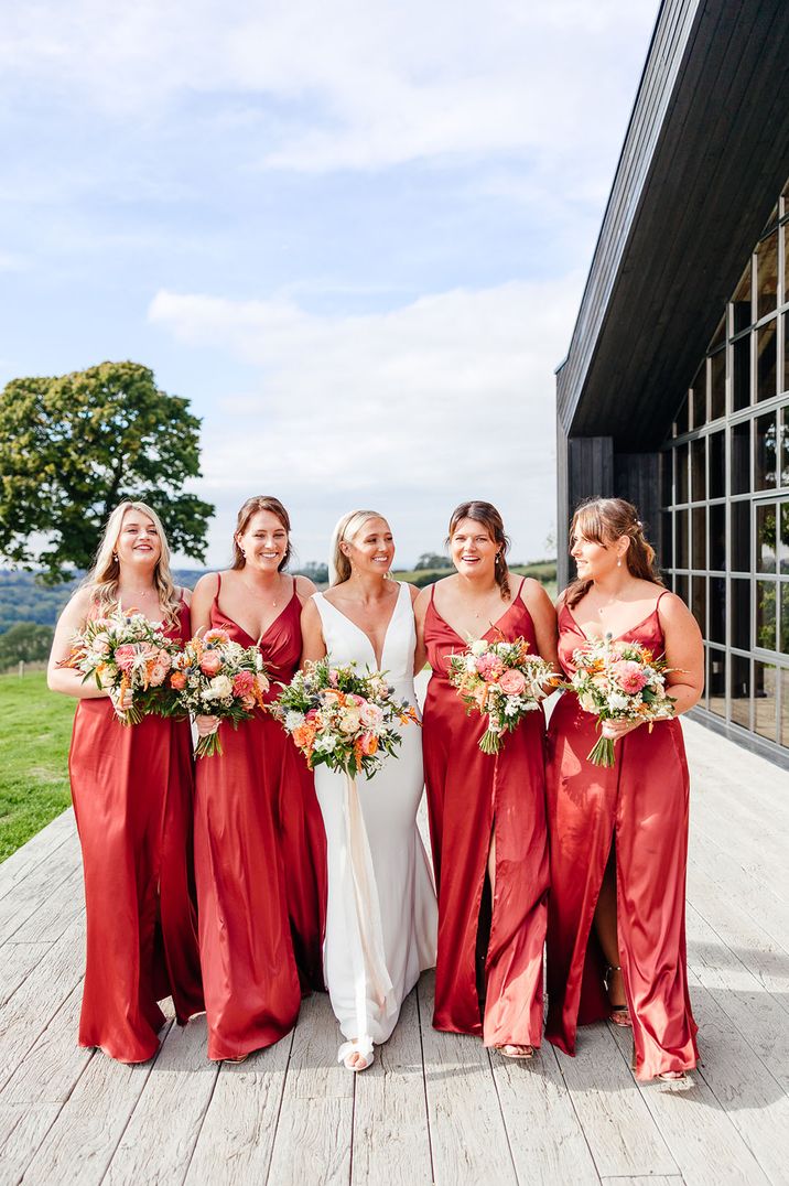 Bridesmaids in red satin bridesmaid dresses walking along The Barn at Botley Hill barn wedding venue 