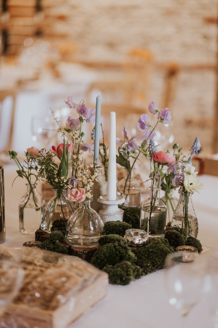 Moss centrepiece decor with ink wells and small vases filled with colourful flowers and taper candles 