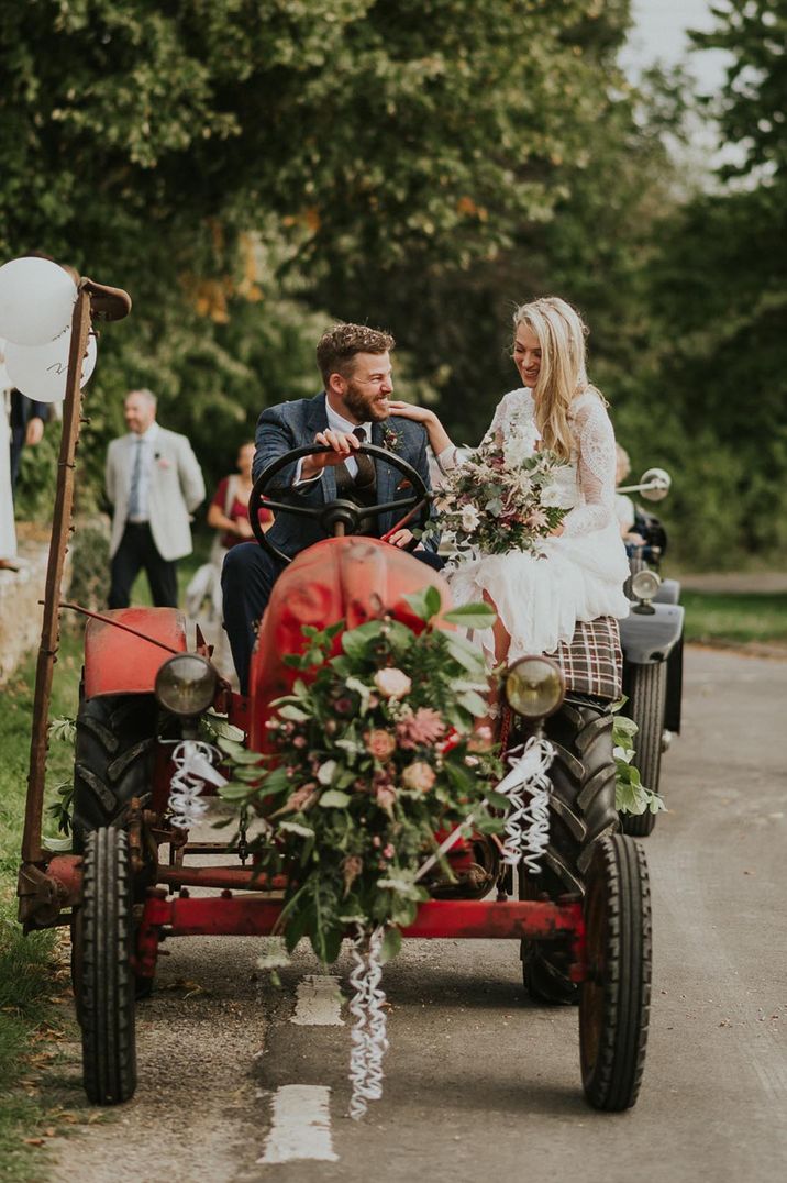 Couple in red tractor wedding transport, bride in long sleeve wedding dress, groom in dark blue suit