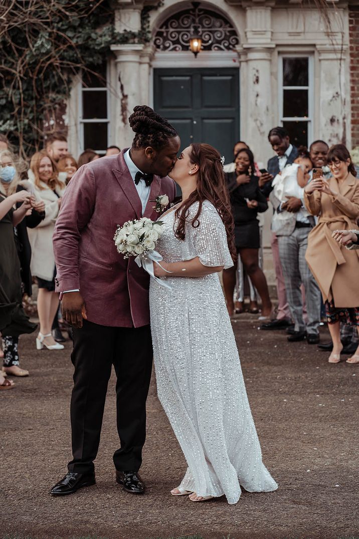 Groom in dusky pink suit jacket kissing the bride in a sparkly silver sequin wedding dress