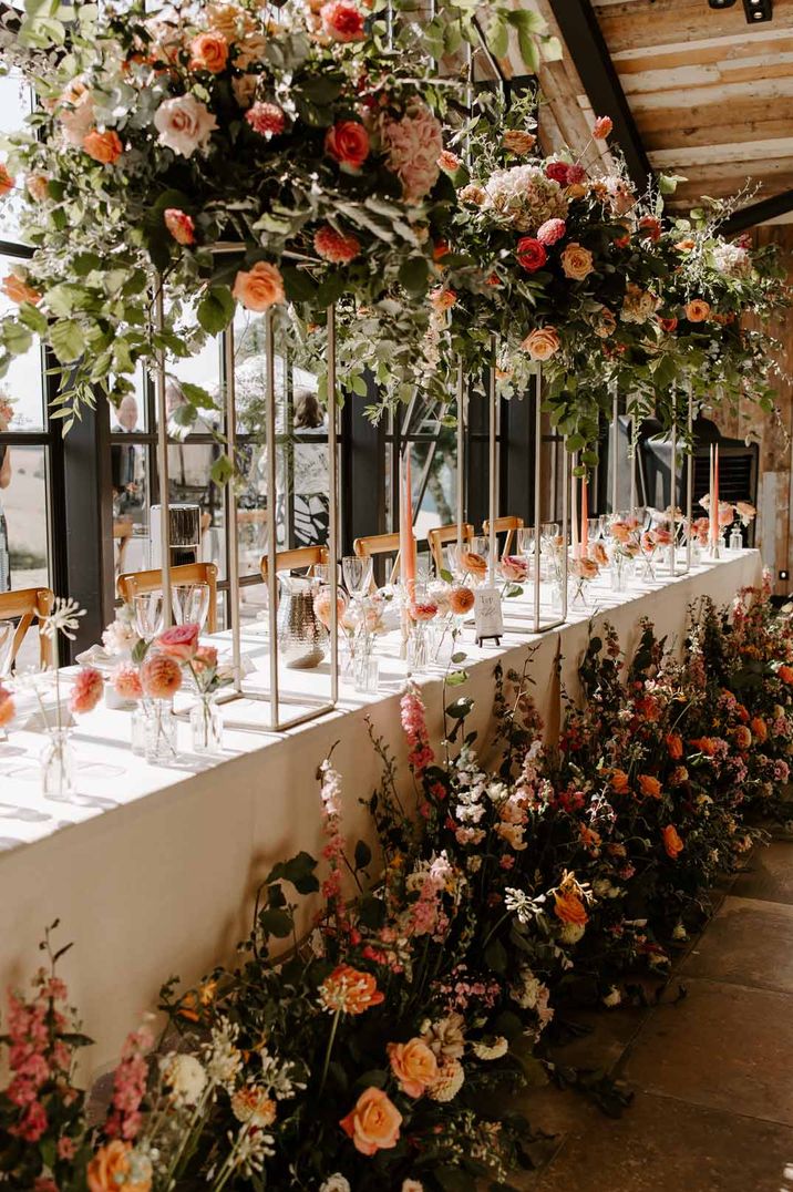 Suspended rose and foliage wedding decorations next to white wedding tablecloth with pink rose centrepieces and tapered candles at Botley Hill Barn - one of the wedding venues London