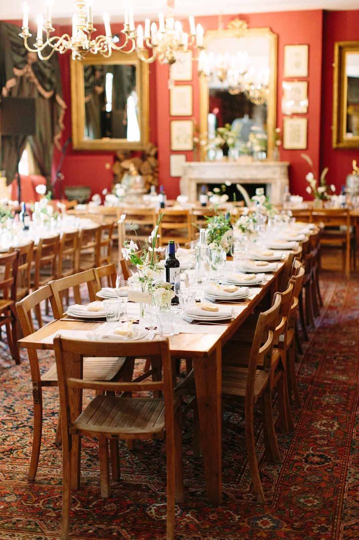 Rustic wedding reception room with wooden tables and chairs, dried flower centrepieces and large gold classic chandeliers 