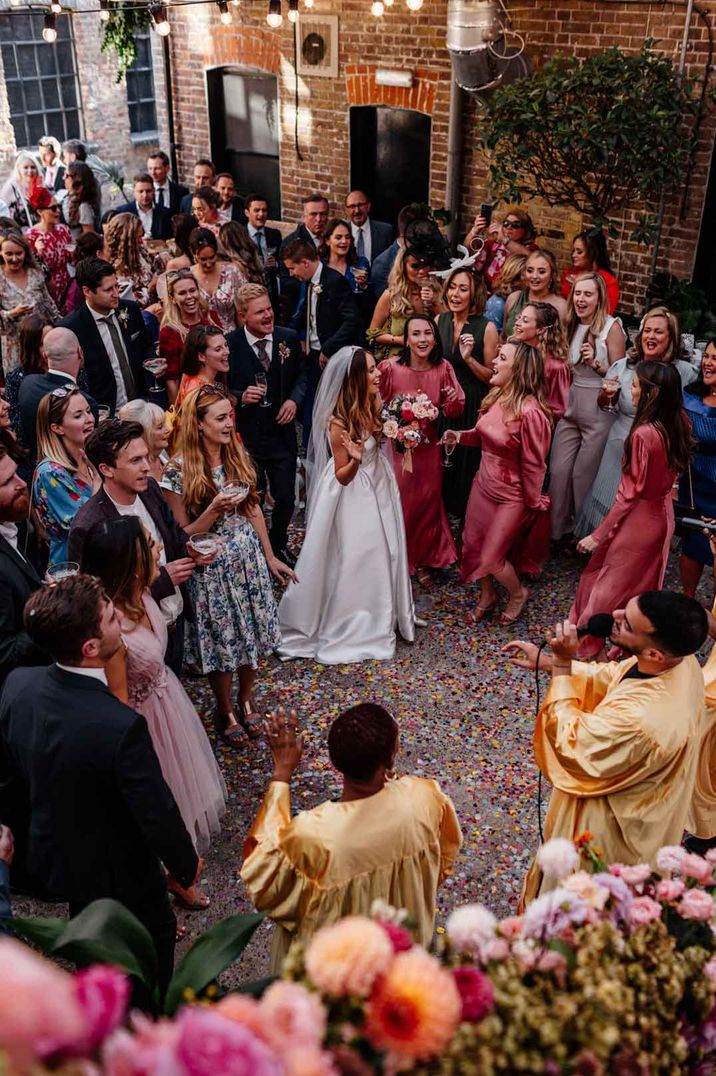 Wedding party celebrating in Loft Studios with confetti, choir singers in gold outfits at Loft Studios - one of the wedding venues London 