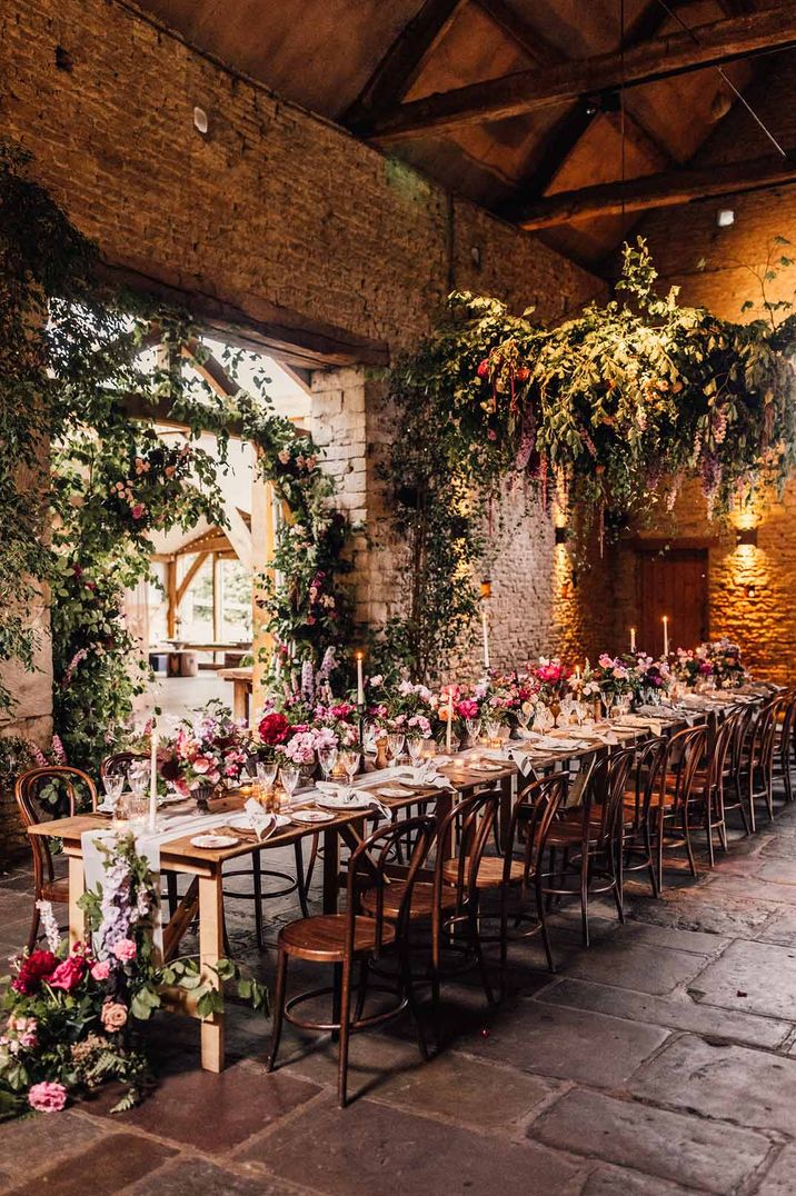 Cripps Barn rustic wedding venue in the Cotswolds with a long banquet table decorated in colourful blooms 