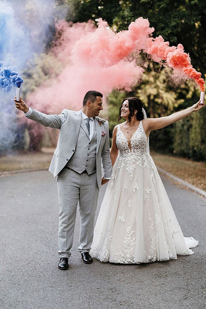 Colourful smoke bomb couple portrait with the bride in a lace wedding dress and groom in a light grey suit 