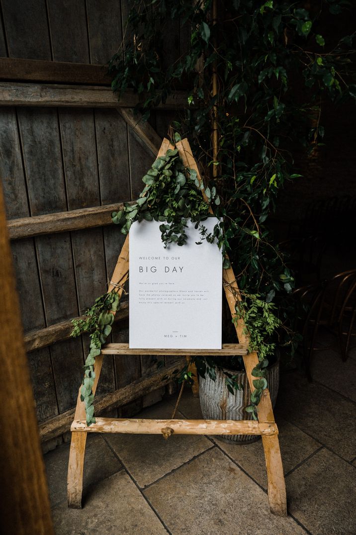 Welcome to our big day wedding sign resting on a rustic wooden easel decorated with ivy 