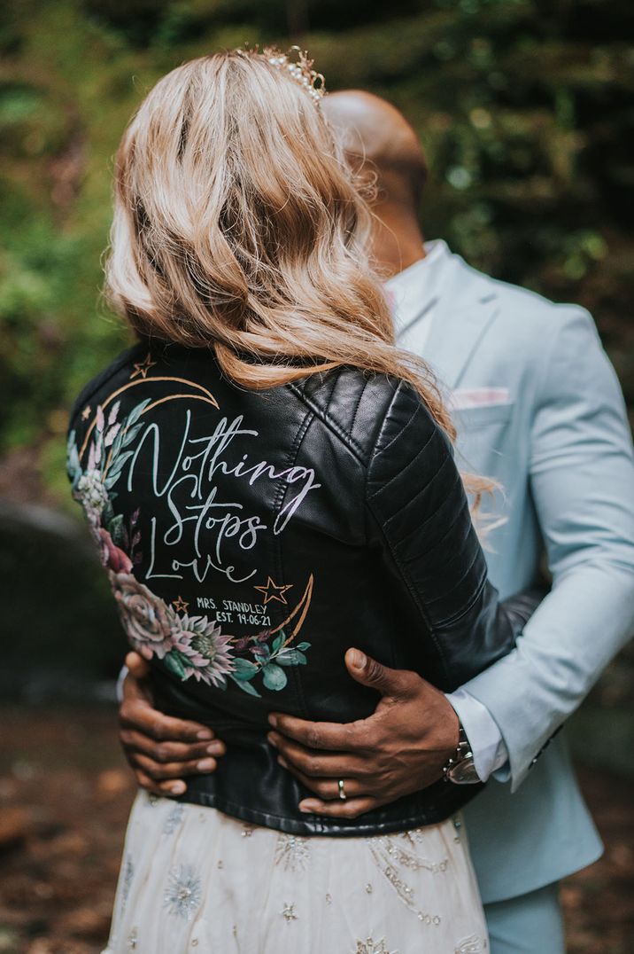 Bride in a custom leather jacket hugging the groom in a pale blue suit 