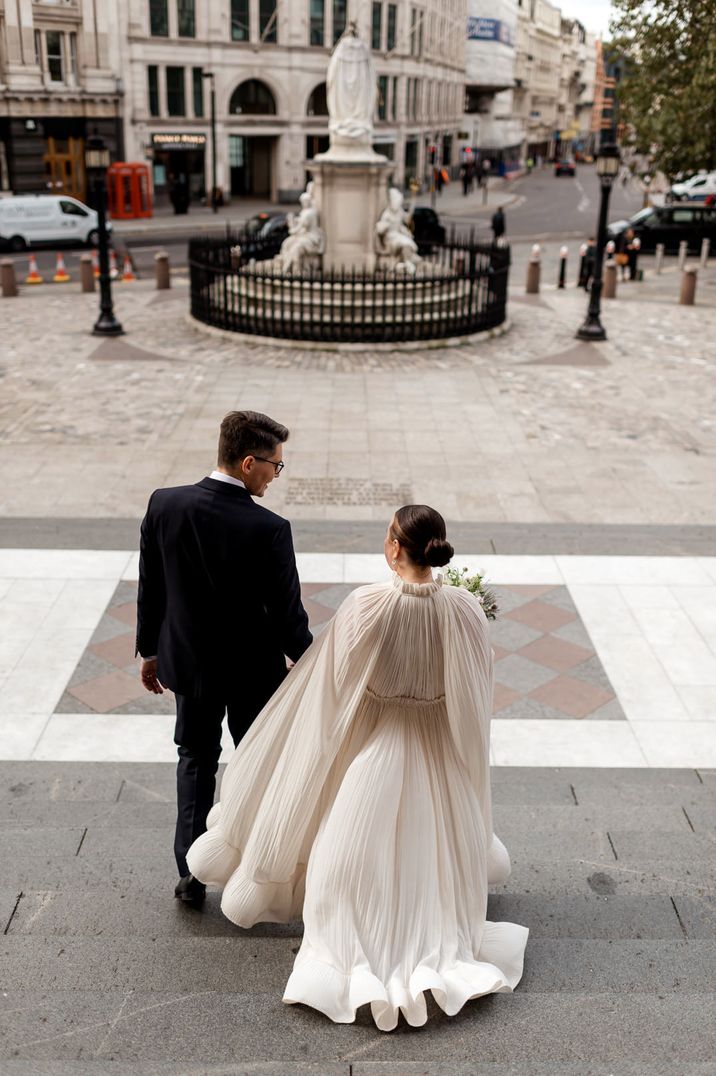 Groom in a blue suit walks down the steps with the bride in a flowing wedding dress 