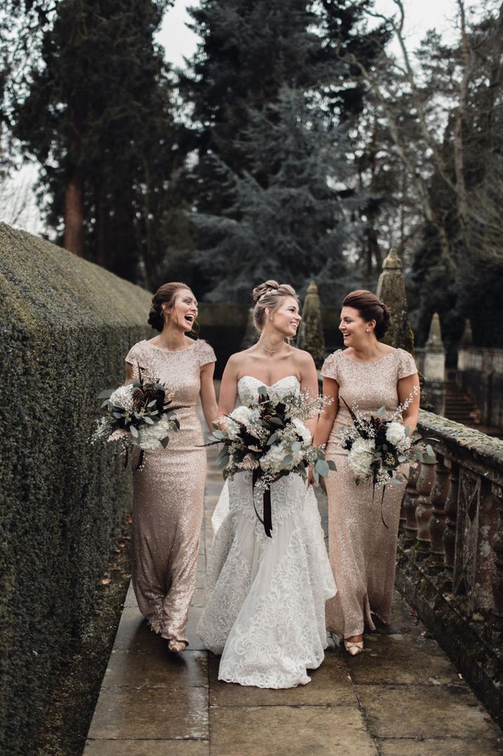 Bride in a strapless lace wedding dress walks with her bridesmaids in gold sequin dresses for a winter wedding 