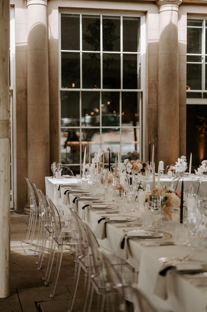 Neutral wedding tablescape with black and cream taper candles with acrylic chairs with pink rose and orchid flower arrangements 