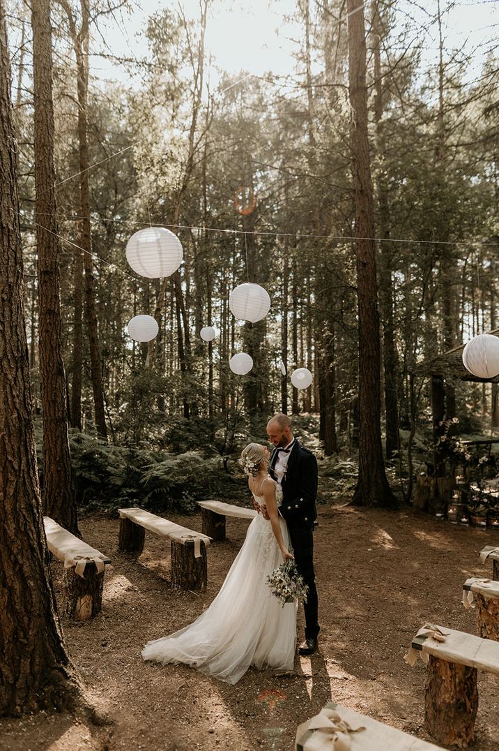 The bride and groom stand in the woodland wedding venue, Camp Katur with white paper lanterns 