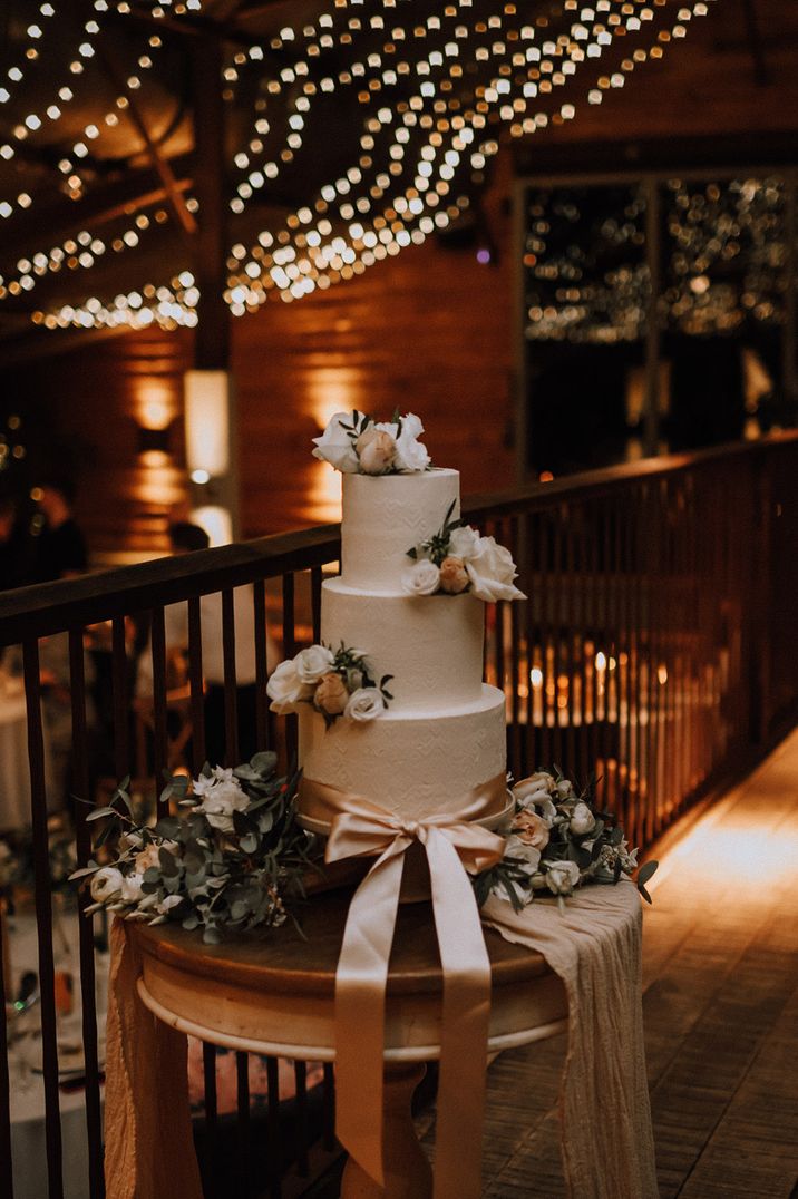 Three tier brocade textured wedding cake with white icing decorated with a light pink ribbon 