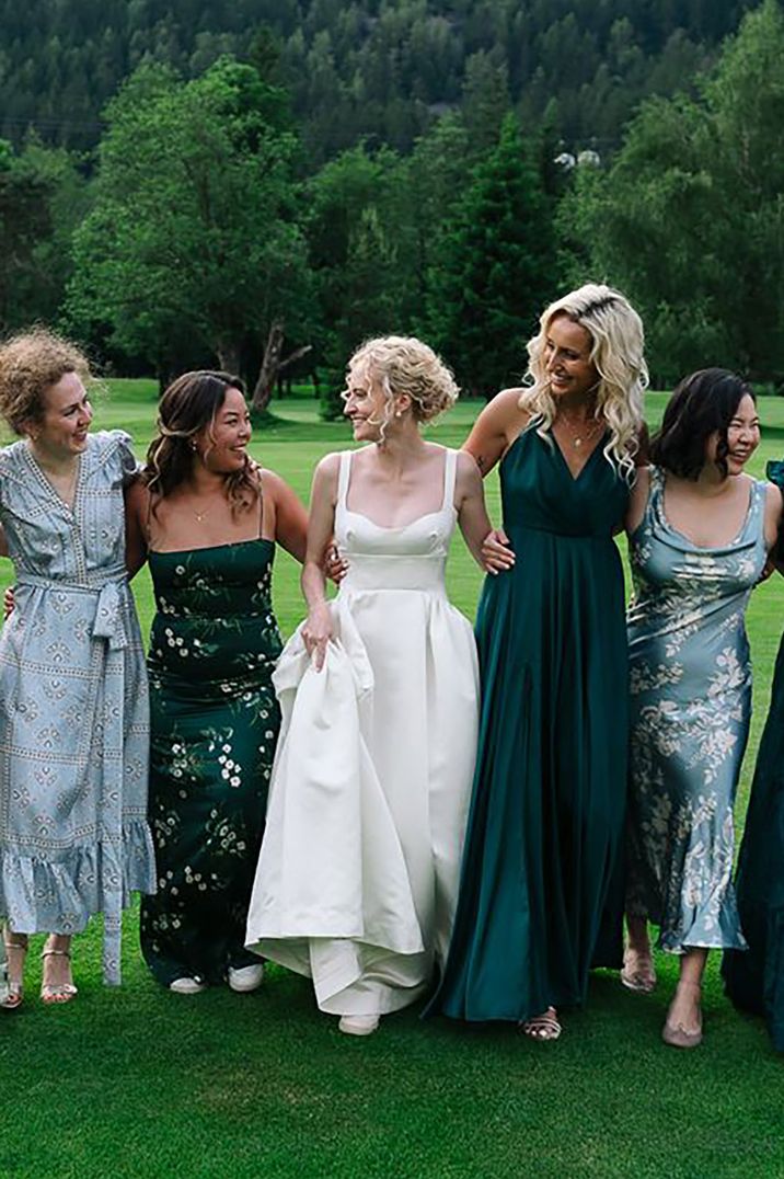 Bride with her bridesmaids wearing green bridesmaid dresses posing for a picture outdoors during Swiss wedding 