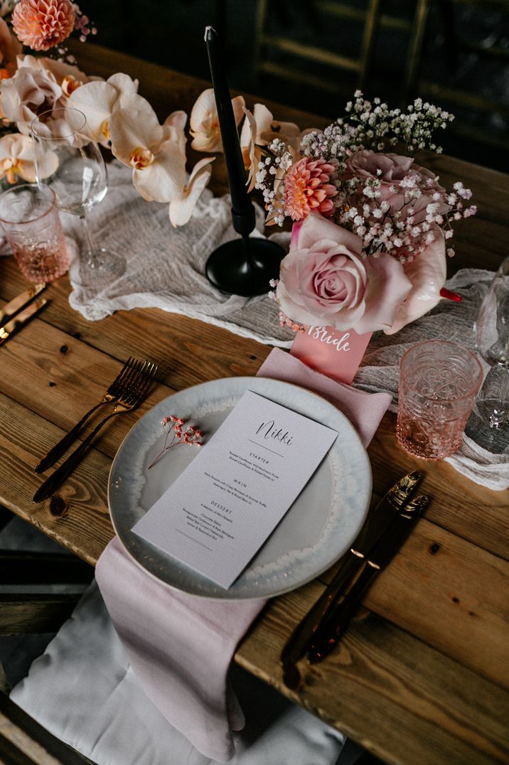 Place setting with gold cutlery and coloured glassware, plus peel back rose centrepieces and black taper candles 