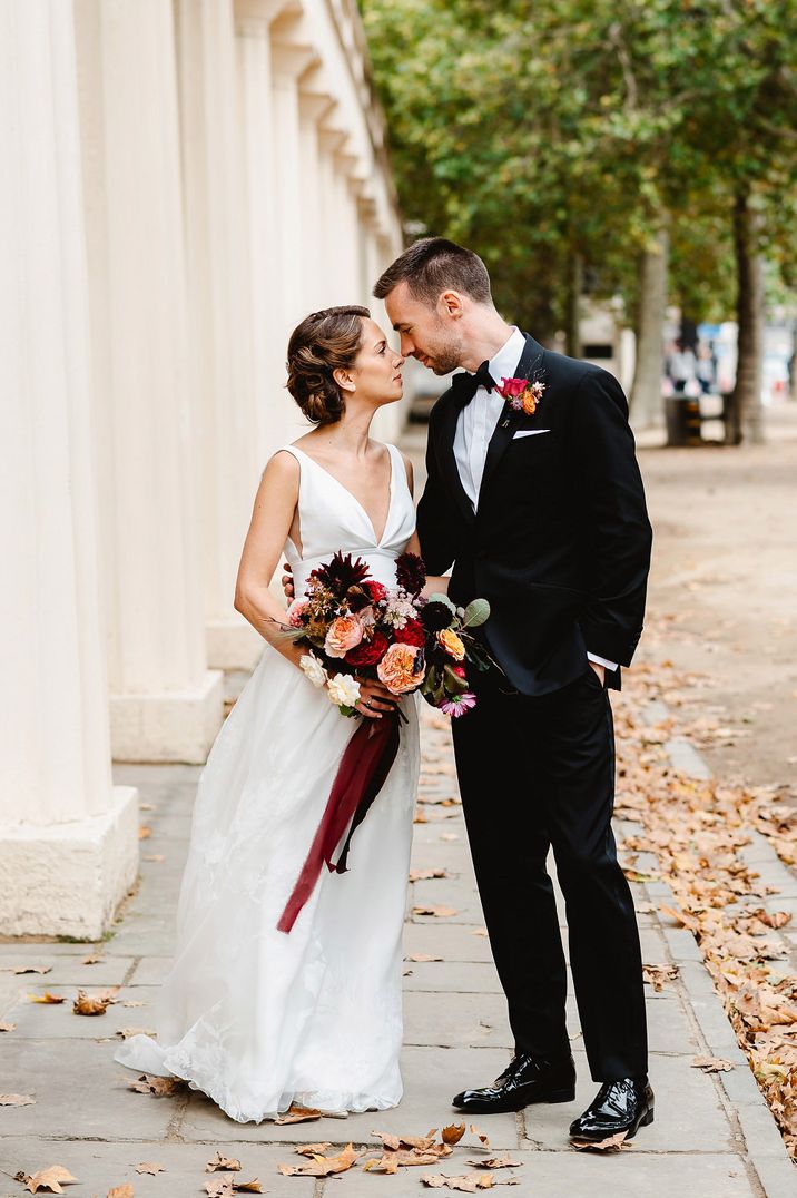 Portrait of the groom in a tuxedo and bride in a Stephanie Allin wedding dress holding a deep red and orange autumn bouquet 