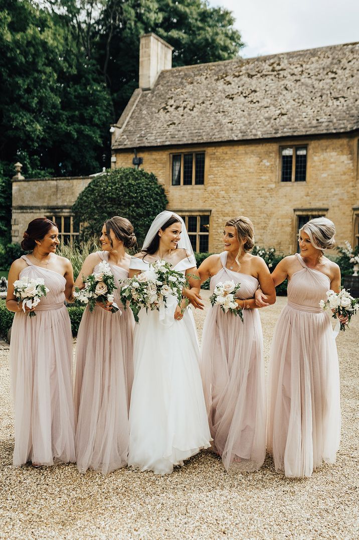 Bridal party in dusky pink bridesmaid dresses and bride in princess wedding dress at traditional wedding