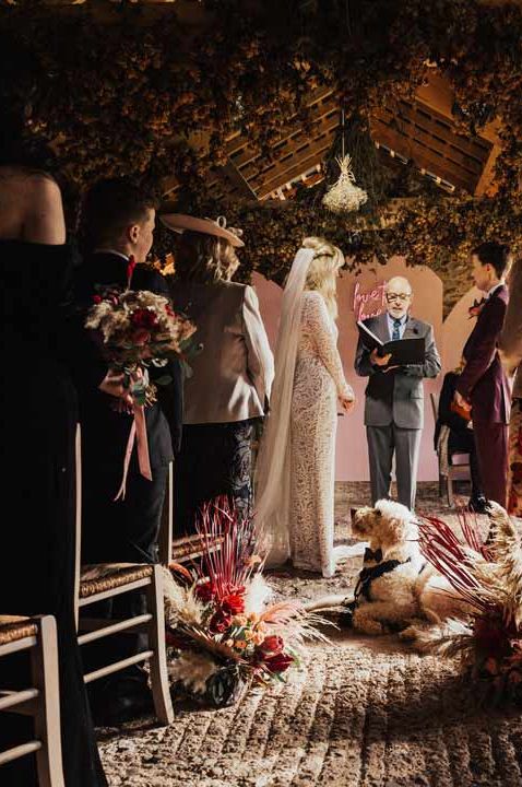 Retro rustic wedding with pet dog ring bearer and happy couple standing reading their vows at the end of the alter